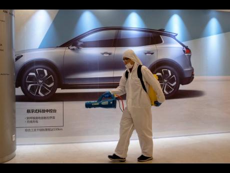In this Februaary 12, 2020, photo, a worker disinfects a mall near an advertisement for a car in Beijing, China.