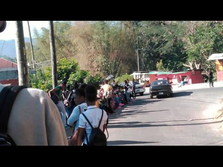 Dozens of students stand along the roadway outside the gates of Oberlin High School in Lawrence Tavern, St Andrew, on Friday. The students were locked out of Jamaica Day celebrations because they wore ripped jeans.