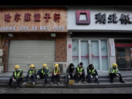 In this Sunday, February 23, 2020 photo, workers take a rest near the closed restaurant and bank in Wuhan in central China’s Hubei province. 