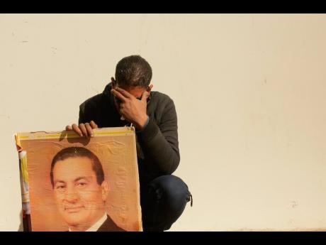 A supporter holds a photo of Egypt’s ousted autocratic President Hosni Mubarak as he weeps outside the gate of the mosque ahead of his funeral in New Cairo, Egypt, Wednesday, February 26, 2020. 