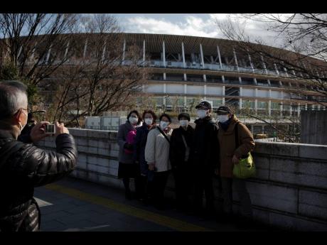 Tourists wear masks as they pause recently for photos with the New National Stadium, a venue for the opening and closing ceremonies at the Tokyo 2020 Olympics.