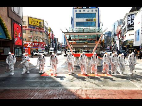 South Korean army soldiers wearing protective suits spray disinfectant to prevent the spread of the COVID-19 virus on a street in Daegu, South Korea, yesterday. As the worst-hit areas of Asia continued to struggle with a viral epidemic, with hundreds more cases reported Thursday in South Korea and China, worries about infection and containment spread across the globe. 