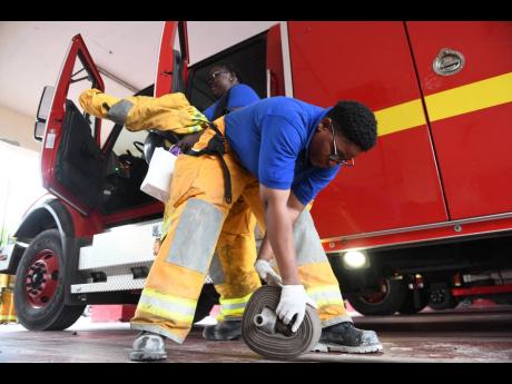 Firefighter Melanie Edwards rolls up a fire hose after returning to the York Park Fire Station, having extinguished a moderate blaze on Wellington Drive in Kingston. Behind her is Corporal Marcia Callum.