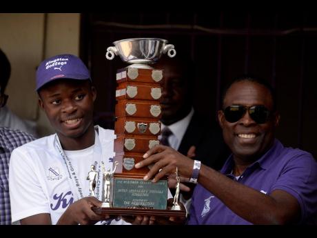 Tarees Rhoden (left), Captain of Kingston College’s 2019 Track Team and Head Coach Leaford Grant (right) show off the Mortimer Geddes Trophy during their 2019 Champs celebration held at Kingston College on April 1, 2019.