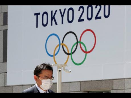 In this Wednesday, March 25,  file photo, a masked man walks in front of a Tokyo Olympics logo at the Tokyo metropolitan government headquarters building in Tokyo. The 2020 Olympics have been moved to next year, but countless questions remain. They revolve around 11,000 Olympic athletes and 4,400 Paralympic athletes. They also include 206 national Olympic committees, sports federations, thousands of contracts, and billions of dollars.