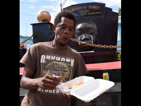 Theo Mullings makes light work of breakfast in front of the Secret Garden monument in downtown Kingston yesterday. Mullings was one of hundreds of homeless persons who were served breakfast during the launch of a special feeding programme in the parking lot of the Kingston and St Andrew Municipal Corporation on Church Street in Kingston.