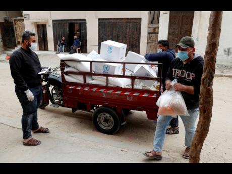 Palestinian workers distribute food supplies from the United Nations Relief and Works Agency for impoverished refugee families after a three-week delay caused by fears of the coronavirus, in the Sheikh Redwan neighbourhood of Gaza City, yesterday. 