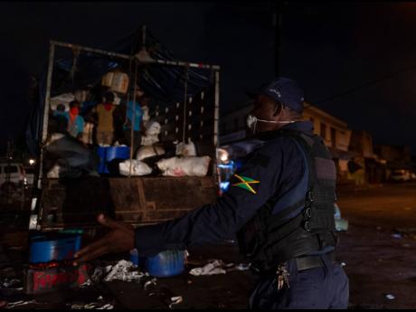 A member of the Jamaica Constabulary Force reprimands men unloading agricultural produce in the vicinity of Coronation Market in downtown Kingston at 8:30 Wednesday night. An all-island curfew under the Disaster Risk Management Act took effect at 8 p.m. yesterday. The 10-hour nightly restriction will run for seven days.