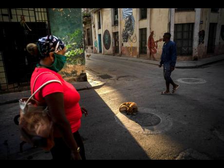 A dog catches the morning sun as he sleeps in the middle of the street, while a woman walks wearing a mask as a precaution against the spread of the coronavirus in Havana, Cuba, on Tuesday, March 31, 2020. Cuban authorities are requiring the use of masks for anyone outside their homes. 