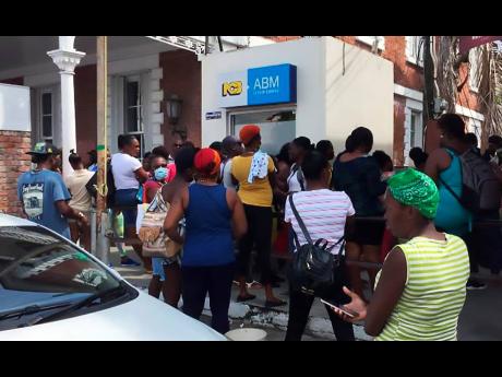 Dozens of people crowd an ATM outside the National Commercial Bank in Port Antonio, Portland, recently. The Government has ordered that commuters stand at least three feet apart to thwart the spread of the novel coronavirus.