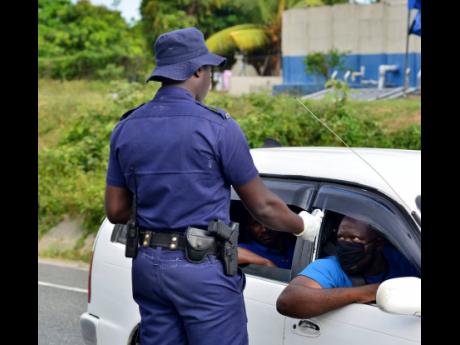 A policeman conducts a temperature check on a motorist in the vicinity of Angels, St Catherine, on Wednesday. 