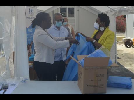 Charmaine Williams-Beckford (left), chief executive officer of the Cornwall Regional Hospital (CRH), is assisted by Janet Silvera (right), president of the Montego Bay Chamber of Commerce and Industry (MBCCI), to get into one of the 50 gowns donated by the MBCCI. Dr Delroy Fray (centre), the CRH’s clinical coordinator, looks on.