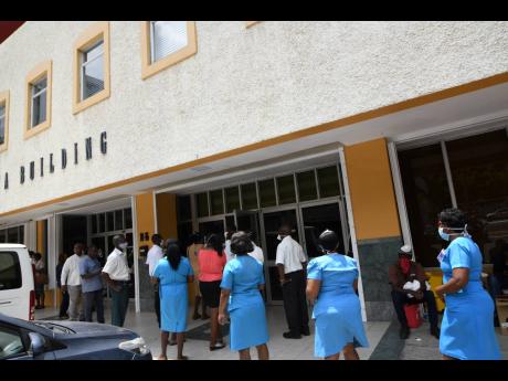 Employees of the Ministry of Health and Wellness stand in a line to enter the RKA Building in New Kingston yesterday, to be interviewed and tested for COVID-19.  A driver who works with the ministry tested positive for the virus. 