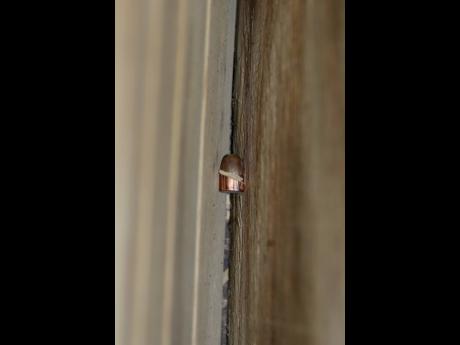 A bullet that went through a window blade before piercing a TV stand is found between sheets of plywood at the Drummond Street home in Denham Town, west Kingston.