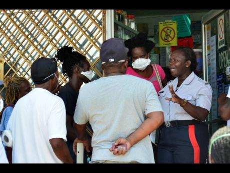 A policewoman tries to calm frustrated customers outside a MoneyGram outlet in Independence City, Portmore, last Saturday. The parish of St Catherine has been placed on a 14-day lockdown. Prime Minister Andrew Holness has warned that criminals are planning to exploit the COVID-19 pandemic for profit by stoking chaos. 