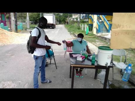 Meliesha Nicholson cleanses the hands of a commuter at an entrance to Brissett district in Lucea, Hanover, last week. A sanitisation post has been established to keep community members free from the new coronavirus. 