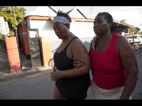 Annette Drummond (left) is supported by Dorrett Robinson, grandmother of Annette’s slain son, Allan Thompson, as she walks along Clarence Road in Craig Town on Saturday. Allan was one of two teenagers killed in a mass shooting in the community.