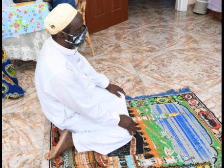 Sheikh Musa Tijani, head of Islamic Education at the Islamic Council of Jamaica, kneels on a prayer mat at home in Vineyard Town, Kingston, on Tuesday.