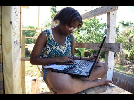 Allana Campbell from Stewart Town in Portland, does school work from her laptop while sitting on a scaffolding at a building under construction. 