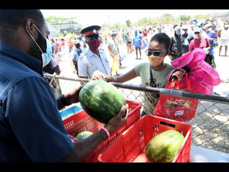 A policeman looks on as a woman purchases a watermelon at the farmers’ market in Barbican, 
St Andrew, yesterday.