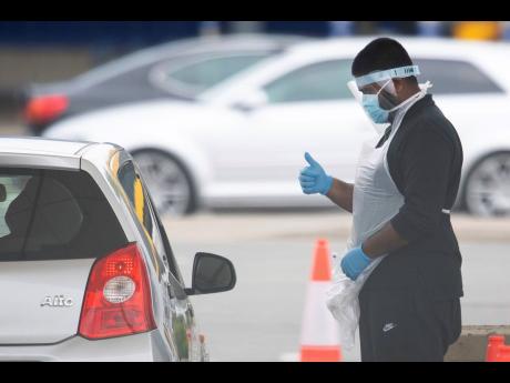 A tester, wearing a mask to protect against the coronavirus, gestures to a driver at a drive-through COVID-19 testing site at IKEA in Wembley, north London, yesterday.