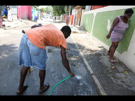 In this photo taken on Tuesday, a resident washes away blood from the spot along Phillip Avenue in Olympic Gardens, St Andrew, where 21-year-old Shannon Staple was murdered on Sunday morning.