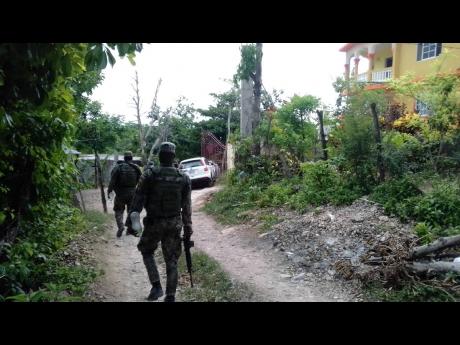 Soldiers are seen outside a house where two men were killed in a gun battle with the security forces in Green Pond, St James, on Monday.