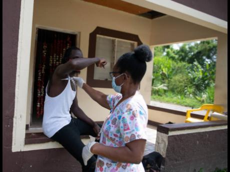 Ricardo Edwards has his temperature taken by Audrey Hinds-McLeod, one of 70 healthcare workers who went on house-to-house visits in Dover, St Mary, on Saturday, May 9.