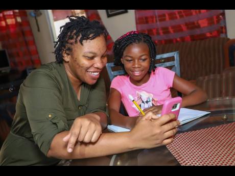 
Krishendale Panton (left), assists her 11-year-old daughter, Cerease McCormack, a grade six student at George Headley Primary School in Duhaney Park, as she continues her studies via the EduFocal online platform using a mobile device at their home.