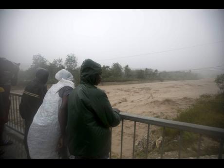 
In this October 4, 2016, photo, people watch rising waters roar past from a bridge in Petit Goave, Haiti, during the passage of Hurricane Matthew. Hurricane activity in 2019 was about 120 per cent of the average season, and 2020 is expected to be even worse at 140 per cent.