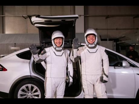 In this Friday, January 17, 2020 photo made available by NASA, astronauts Doug Hurley (left) and Robert Behnken pose in front of a Tesla Model X car during a SpaceX launch dress rehearsal at the Kennedy Space Center in Cape Canaveral, Florida.