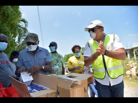 Health and Wellness Minister Dr Christopher Tufton (right) sanitises his hands before examining personal protective gear and other items donated to the Corn Piece community in Clarendon. Meanwhile, Member of Parliament for South East Clarendon Pearnel Charles Jr (second left) looks at a box containing face masks. 