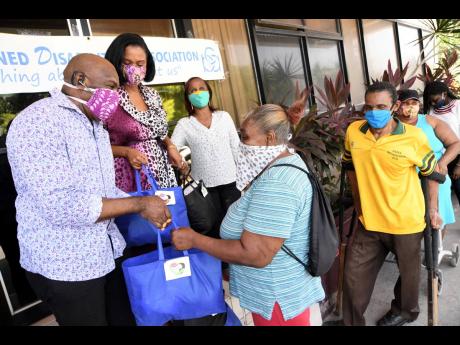 Senator Floyd Morris; his wife, Shelley-Ann (second left); and Gloria Goffe (third left), executive director of the Combined Disabilities Association of Jamaica, hand out packages and supplies to people with disabilities. Collecting her package is Lorna Pinnock while Errol Williams (second right) and Denise Wray await their turn at the Combined Disabilities offices at 18 Ripon Road on Tuesday of this week.