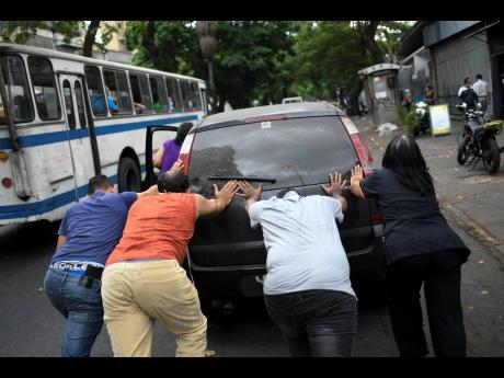 People push a car that ran out of gas to a state-run oil company PDVSA filling station in Caracas, Venezuela, yesterday. The first of five tankers loaded with gasolene sent from Iran this week is expected to temporarily ease Venezuela’s fuel crunch while defying Trump administration sanctions targeting the two US foes. 