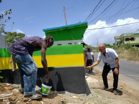 Mayor of Morant Bay, Michael Hue, paints a garbage receptacle in Leith Hall, St Thomas, on Labour Day yesterday.