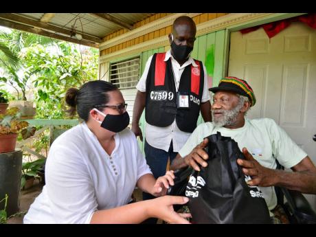 Saffrey Brown (left), chairman of the Council of Voluntary Social Services, and Deputy Superintendent Rory Martin deliver a care package to Joseph Heslop, who is unable to walk, in the community of Central Village, 
St Catherine, on Saturday. The distribution drive was part of the PSOJ’s COVID-19 relief programme.