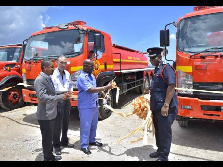 In this 2018 Gleaner photo, Minister of Local Government and Community Development Desmond McKenzie (third left) cuts the ribbon symbolising the official handover of four new fire trucks to the Jamaica Fire Brigade in Kingston. Others sharing in the moment