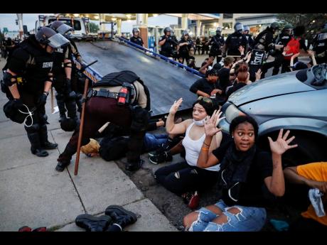 Protesters raise their hands on the command of the police as they are detained prior to arrest and processing at a gas station on South Washington Street, Minneapolis, on Sunday, May 31. The protests were sparked by the death of George Floyd, who died afte