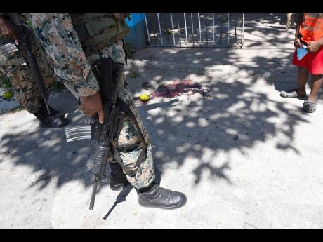 Jamaica Defence Force soldiers stand near the bloodstained ground where the body of one of two brothers shot and killed by gunmen was found along Payton Place in August Town on Wednesday.