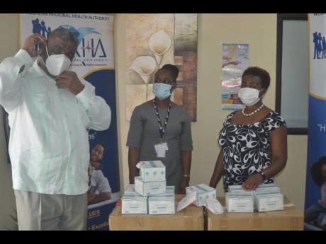Errol Greene (left), regional director of the Western Regional Health Authority, tries on one of the 6,000 N95 face masks donated to his organisation by the Global Services Association of Jamaica (GSAJ) yesterday. Looking on are  Gloria Henry (right), GSAJ
