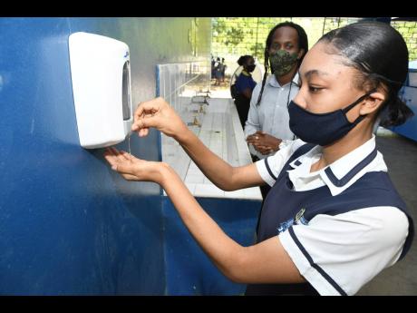 Junior Education Minister Alando Terrelonge looks on as Cedar Grove Academy student Lechelle Walker sanitises her hands yesterday as schools across the island reopened to students sitting external examinations.