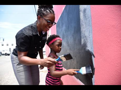 Aisha Campbell (left), CEO of Proven REIT, and six-year-old Taneemar Phipps as they paint a community blackboard in Tavares Garden. Proven donated paint and school supplies to the children of Tavares Gardens, Delacree Lane, and other surrounding communitie