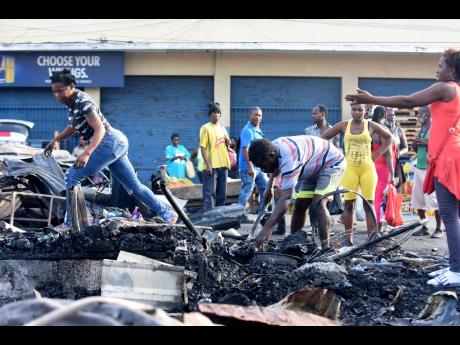 Distraught vendors sift through charred rubble yesterday after fire destroyed the Rae Rae Market in downtown Kingston overnight. 