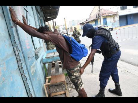 A cop searches a passer-by at a state of emergency checkpoint at North Street in central Kingston moments after Prime Minister Andrew Holness announced a 14-day crackdown in the Kingston Western and Central police divisions on Sunday.