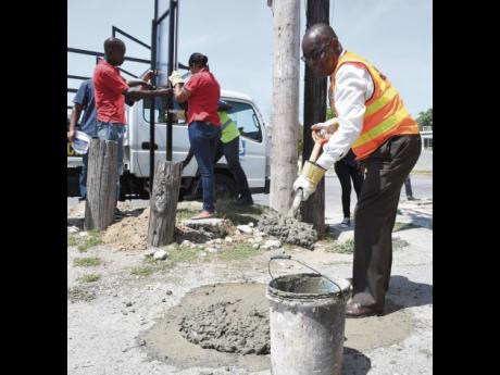 Leon Thomas (right), mayor of Portmore, mixes mortar to erect a sign that directs Portmore citizens to the evacuation route in case of an emergency. The Portmore Municipality erected 10 signs across Portmore, costing over J$950,000, on Tuesday, June 16.
