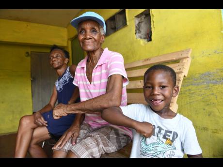Ann-Marie Nichols (left), 65, and Gloria Mendez, 83, is greeted by her great grandson five-year-old Jovane Gallimore, while speaking about their concerns with the recent cases of COVID-19 in their community. Personnel from the Ministry of Health & Wellness