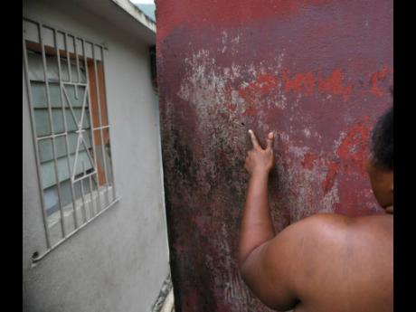 A woman shows bullet holes in a wall at premises on Bryce Hill Lane in August Town, St Andrew, on Tuesday. A family residence has been shot up twice in as many days, with three people sustaining gunshot wounds.