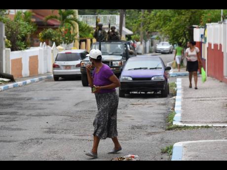 A woman crosses a street as a Jamaica Defence Force patrol approaches moments after a zone of special operations was declared in August Town, St Andrew, yesterday.