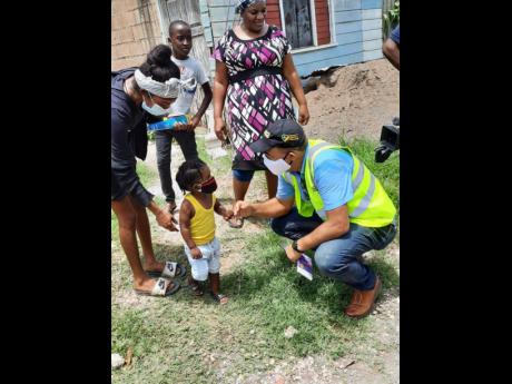 Minister of Health and Wellness Dr Christopher Tufton engages with a toddler in the Bottom Town community, Clark’s Town, Trelawny, last Friday, while other residents look on. Occasion was a sensitisation walk in the community, which has two imported case
