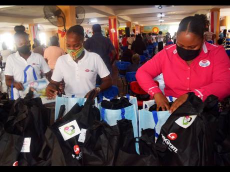 LASCO Financial Services Limited’s Sponsorship and Promotions Officer, Nikeisha Alexander (right,) and LASCO Money brand ambassadors prepare donation packages filled with personal care and food items for Break Through PHD Ministries during a handover ses